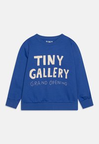 Niebieska bluza z bawełny, z okrągłym dekoltem i długimi rękawami. Na przodzie znajduje się nadrukowany tekst "TINY GALLERY GRAND OPENING" w kolorze beżowym.