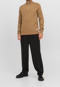 Brun ribbad polotröja med en fjärdedels dragkedja, bärs tillsammans med svarta vida byxor och svarta snörskor. Enkel logotyp på tröjan.