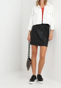 Veste en denim blanc raccourcie sur un haut rouge, associée à une jupe en simili cuir noir. Baskets noires sans lacets et sac à main à bandoulière.