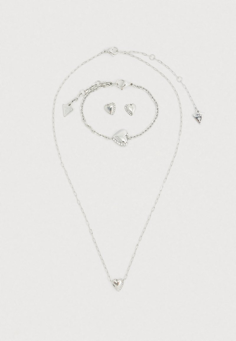 Ensemble de bijoux en argent comprenant un collier, un bracelet et des boucles d'oreilles avec des formes de cœur, des motifs texturés et de petits accents de strass.