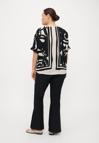 Blusa nera e beige a maniche corte con motivi astratti, abbinata a pantaloni neri a zampa d'elefante e sandali con cinturini. Tessuto di consistenza liscia.