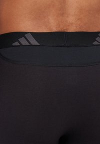 Leggings atléticos pretos com um design ajustado e uma cintura larga e elástica, apresentando um logo da marca em cinza escuro na parte de trás.