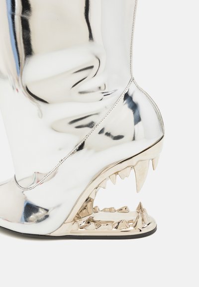 Metallic silver knee-high boot with a sculpted gold shark jaw heel featuring jagged teeth and a sleek, shiny outer texture.