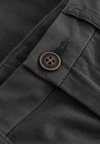 Tissu gris foncé avec une texture lisse, présentant un bouton avec un détail de logo gravé et des coutures plates sur le côté droit.
