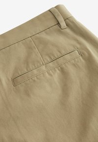 Khakifärgade byxor i ett slätt, strukturerat tyg, med en enkel bakficka med en platt design och subtila sömdetaljer.
