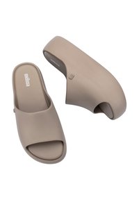 Sandali slide arrotondati in morbido materiale beige con punta aperta, texture liscia e un logo discreto sulle solette.