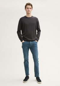 Camisa de manga larga gris oscuro combinada con jeans azules. La camisa tiene un escote redondo y una textura suave, mientras que los jeans tienen un corte clásico.