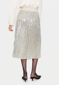 Fodrad silverpailletty midi kjol med en mjuk, elastisk midjeband. Tyget har en glänsande, texturerad yta som reflekterar ljus.