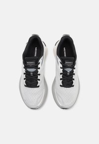 Zapatillas deportivas ligeras en malla blanca y negra con una suela gris acolchada, que presentan cordones negros y detalles reflectantes.