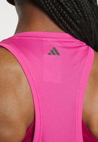 Canotta sportiva rosa con design in rete traspirante, cuciture piatte e un piccolo logo Adidas nero sulla spalla.