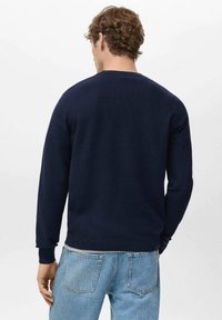 Marineblauer Strickpullover mit Rundhalsausschnitt und gerippten Bündchen, getragen über hellblauen Jeans, zeigt eine glatte Textur und schlichtes Design.