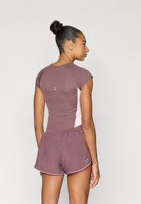 Μπορντό αθλητική μπλούζα με κοντά μανίκια σε συνδυασμό με μπόρντο σορτς που ταιριάζουν. Η μπλούζα έχει ανοιχτό ροζ πλευρικό πάνελ και διακριτικές λευκές λεπτομέρειες.