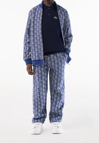 Tuta blu con motivo, composto da una giacca bomber con zip e pantaloni abbinati, realizzato in morbido tessuto con polsini e colletto a costine. Sneakers bianche.