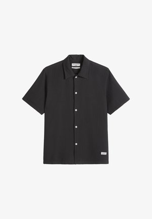 Black short-sleeve button-up shirt with a collar, white buttons down the front, textured fabric, and a small label near the bottom hem.