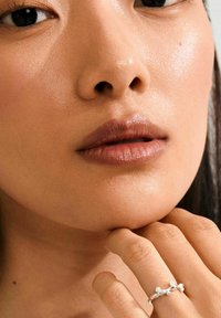 Silver ring with delicate, rounded accents. Close-up of a person's face and hand, featuring smooth skin and natural lip color.