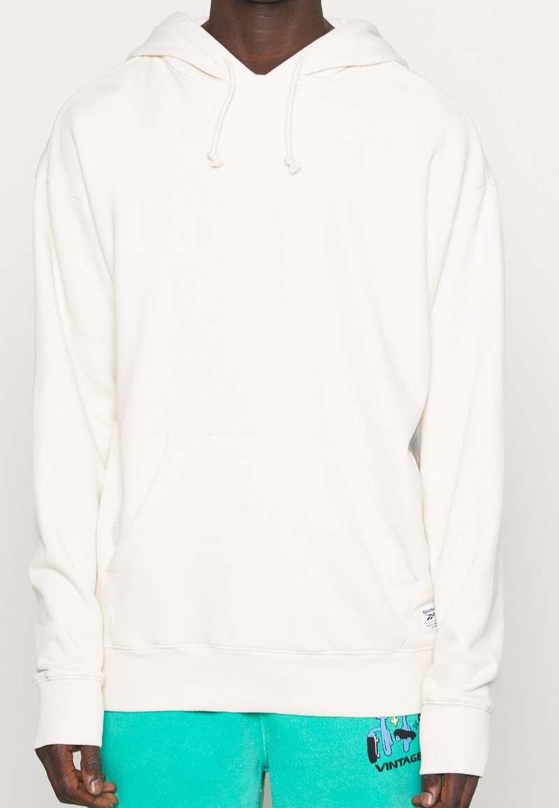 Krämfärgad hoodie med en ficka, dragsko i huvan, ribbade ärmslut och nederkant. Tillverkad av mjukt tyg, har en minimalistisk design.