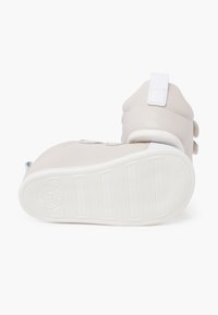 Scarpe in pelle beige con punta arrotondata, dotate di due strap in velcro, un collare imbottito e una suola in gomma bianca con scanalature verticali.
