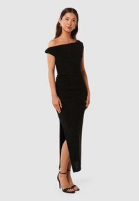 Rochie neagră, fără umeri, cu un design ajustat, fante pe lateral și țesătură texturată. Asortată cu sandale negre cu barete.