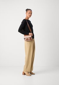 Schwarzer Strickpullover, beigefarbene weite Hosen und tanfarbene Absatzstiefeletten. Braune, kroko-embossierte Umhängetasche mit Klappenverschluss.