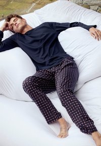 Marineblauwe lange mouw top gecombineerd met een pyjamabroek met een donker achtergrond en geometrische motieven in rood en wit. Losse pasvorm, zacht materiaal.