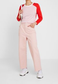 Czerwono-różowa koszula z długim rękawem i okrągłym dekoltem, zestawiona z jasnoróżowymi spodniami. Dopełnieniem stroju są masywne białe trampki.