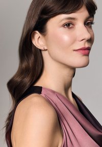 Sukienka z jedwabiu w gradientzie różu i ciemnej śliwki, z tkaniną w drapowanym stylu, czarnym wykończeniem na ramieniu oraz minimalnymi srebrnymi kolczykami w kształcie obręczy.