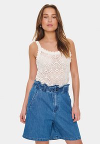 Top croșetat alb cu margini ondulate, asociat cu pantaloni scurți din denim albastru, lejeri, cu talie cu curea și buzunare frontale.