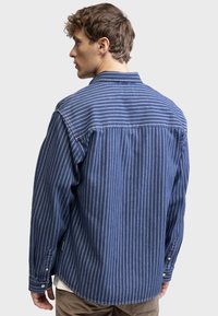 Blue striped shirt with a button-down collar, long sleeves, and a relaxed fit. Fabric texture appears soft and slightly textured.