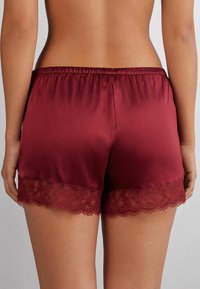 Pantalones cortos de satén burdeos con una suave cinturilla elástica y detalles de encaje en el dobladillo, que cuentan con una textura lisa y un ajuste relajado.