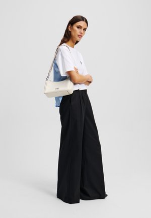 Camiseta blanca combinada con pantalones amplios negros. Un bolso color crema con un acabado texturizado, llevado tipo bandolera, descansa en el costado.