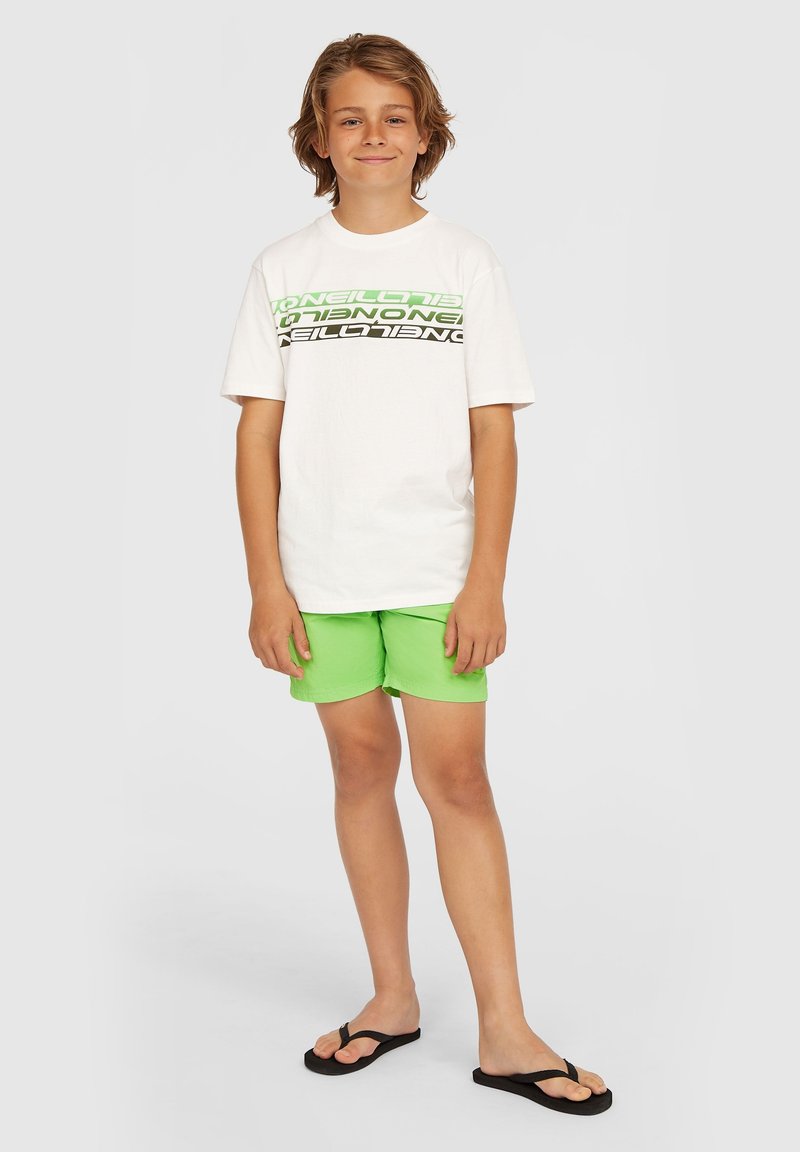 Witte t-shirt met grote zwarte en neon groene tekstpatronen. Heldere groene shorts en zwarte flip-flops maken de outfit compleet.