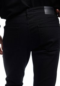 Vaqueros negros de denim, con una textura suave, diseño de cinco bolsillos y un parche de cuero en la parte posterior. El ajuste es ceñido al cuerpo.