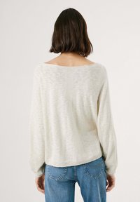 Maglione beige leggero in maglia con una vestibilità ampia, scollo largo e maniche lunghe, abbinato a jeans in denim blu. Tessuto morbido e dalla texture piacevole.