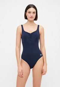 Maillot de bain une pièce bleu marine avec un corsage froncé, des bretelles larges et une jambe haute. Fabriqué en tissu lisse et extensible, avec un accent de logo.