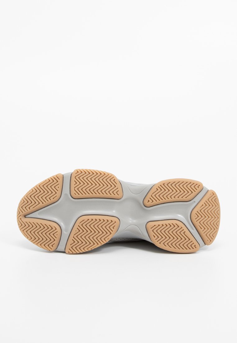 Suela de zapato deportivo gris claro con un patrón de tracción de goma; los acentos de goma texturizada crean contraste. Forma redondeada para mayor comodidad y soporte.