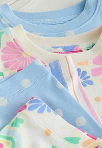 Chemises pour enfants en coton doux empilées, présentant un bleu pastel avec des pois blancs et des motifs floraux en rose, bleu, vert et orange.