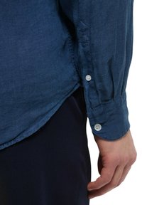 Camicia di lino blu scuro con maniche lunghe, polsini abbottonati e una consistenza morbida, caratterizzata da un orlo dritto e dettagli di cucitura sottili.