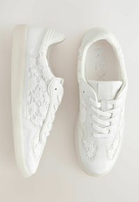 Hvide sneakers med en snøre-overlæk, strukturerede læderdetaljer, rund tå og flad, gennemsigtig gummisål med snørebåndsdesign.