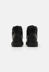 Schwarze Stiefeletten aus einer Mischung aus glattem Leder und strukturiertem Stoff, mit einem Logodetail auf der Rückseite und einer robusten Profilsohle.