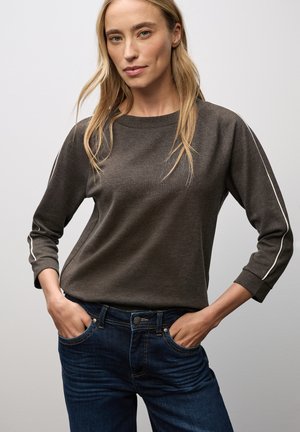 Lichtgewicht donkergrijze langemouwtop met witte zijkanten, gecombineerd met strakke blauwe jeans met klassieke zakken en een knoopsluiting.