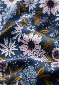 Modrá látka s květinovým vzorem, na které se nacházejí velké růžové a bílé květy, tmavá centra a zelené listy. Jemná textura s detailními prvky.
