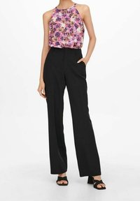 Top sin mangas de flores en tonos púrpura y rosa, combinado con pantalones de cintura alta negros. Los pantalones tienen un corte recto y bolsillos.