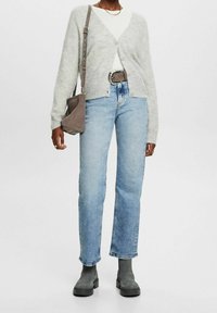 Cárdigan gris claro sobre una blusa blanca de canalé, combinado con jeans rectos azul claro y botas de tobillo grises, junto con un bolso cruzado gris.