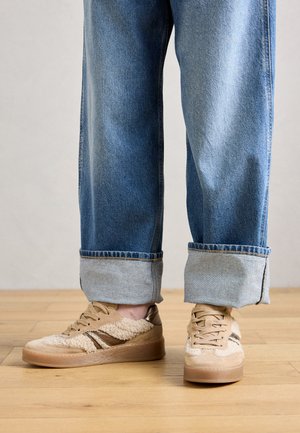 Baskets beiges avec une superposition de fourrure texturée, des accents en cuir marron et une semelle en caoutchouc. Portées avec un jean en denim bleu à large revers.