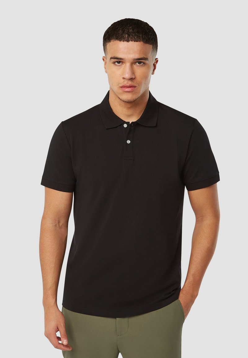 Zwarte polo met een kraag, drie knopen aan de voorkant en korte mouwen, gemaakt van een gladde stof, gecombineerd met olijfgroene broek.