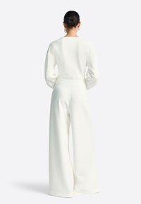 Balta, ar garām piedurknēm, virsjaka un plata piegriezuma bikses, abas izgatavotas no mīksta, gluda auduma. Tops ir ar apaļu apkakli un brīvu piegriezumu.