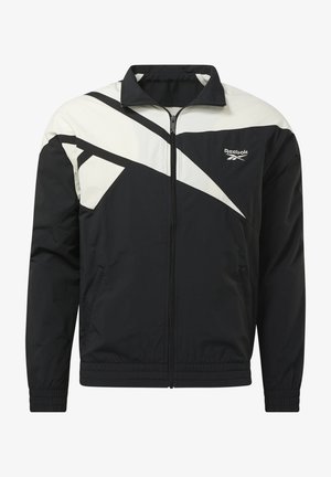 Chaqueta Reebok negra y blanca con cremallera, cuello alto, diseño diagonal de bloques de color y puños y dobladillo elásticos.