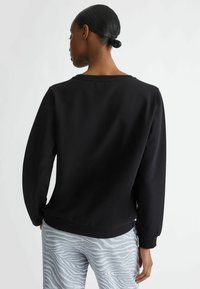 Felpa nera con collo rotondo e maniche lunghe. Texture liscia e vestibilità comoda, abbinata a pantaloni grigio chiaro con fantasia.