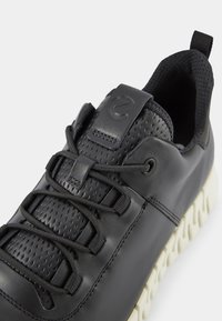 Czarne sneakersy z teksturowaną skórzaną cholewką, z wiązaniami i gumową podeszwą. Posiadają logo na języku oraz kontrastowe przeszycia.