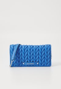 Modrá prošívaná peněženka s tkaným vzorem, která obsahuje odnímatelný popruh, stříbrné kování a na přední straně je vyražená značka.